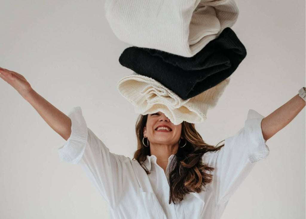 Smiling woman playfully tossing black and white knit sweaters in the air. Clothing organization fun.