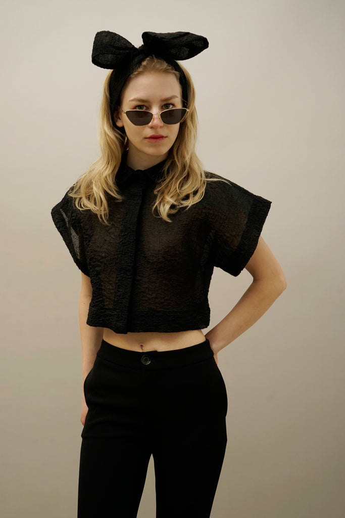 Woman wearing black textured cropped blouse with short sleeves, high-waisted black pants, sunglasses, and oversized bow headband