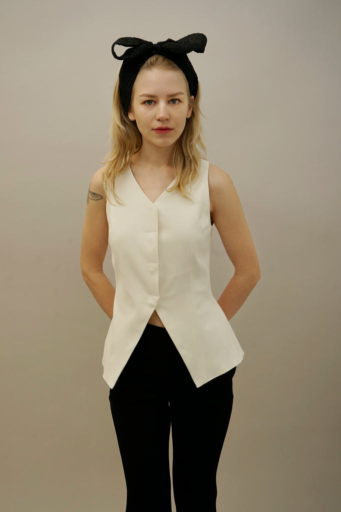 Elegant white sleeveless top with a tailored fit, worn with classic black pants and a trendy black bow headband, highlighting minimalist style.