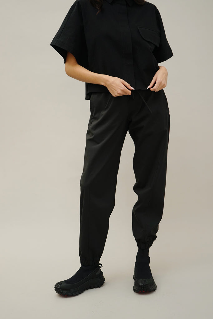 Women's modern black joggers with elastic waist and ankles, featuring sleek waterproof tech fabric for outdoor wear.