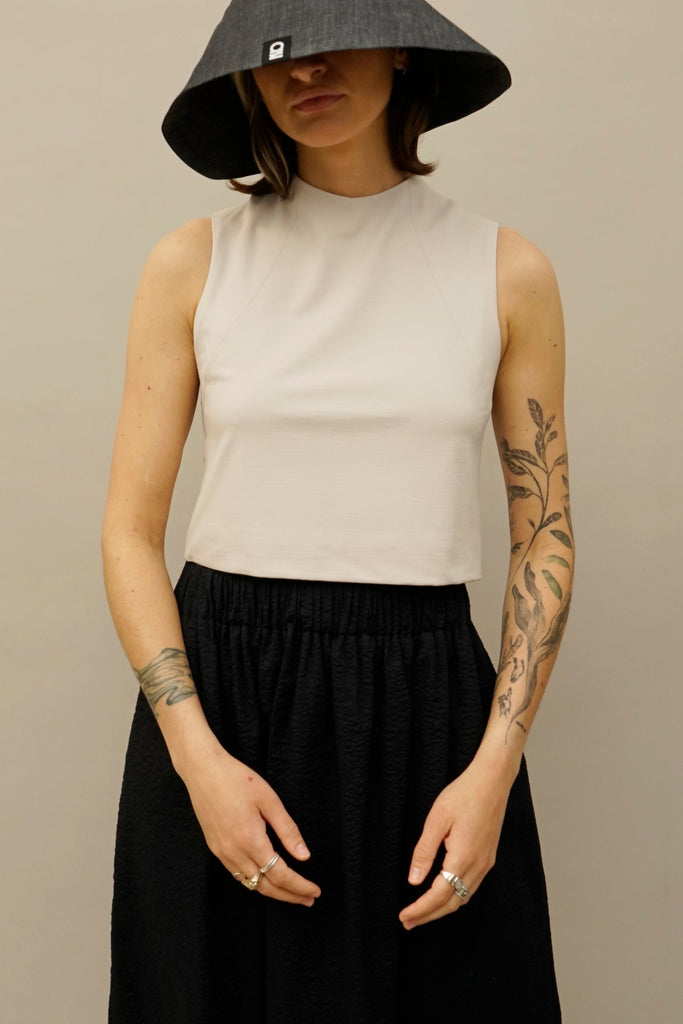 Model wearing sleeveless tan crop tailored top and black textured skirt from NINObrand, styled with wide-brim denim hat.