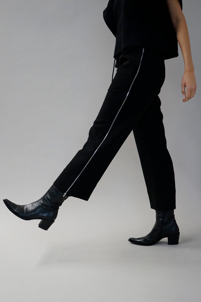 Side profile of black tailored wide-leg pants with subtle textured details, complemented by a matching cropped jacket and pointed-toe boots.