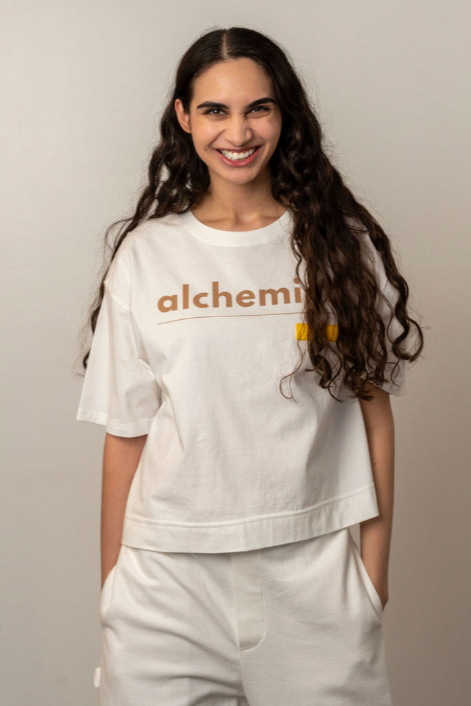 Woman wearing a white oversized Unbranded t-shirt with 'alchemist' graphic text, styled with lounge pants by NINObrand