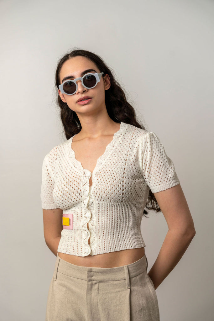Woman wearing a cream knit cropped cardigan with ruffle trim and beige trousers