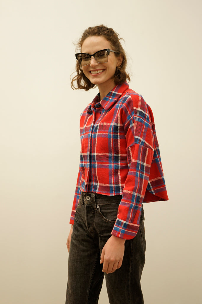 Model wearing cropped red plaid flannel shirt with blue and white stripes by NINObrand, styled with high-waisted black jeans and cat-eye sunglasses