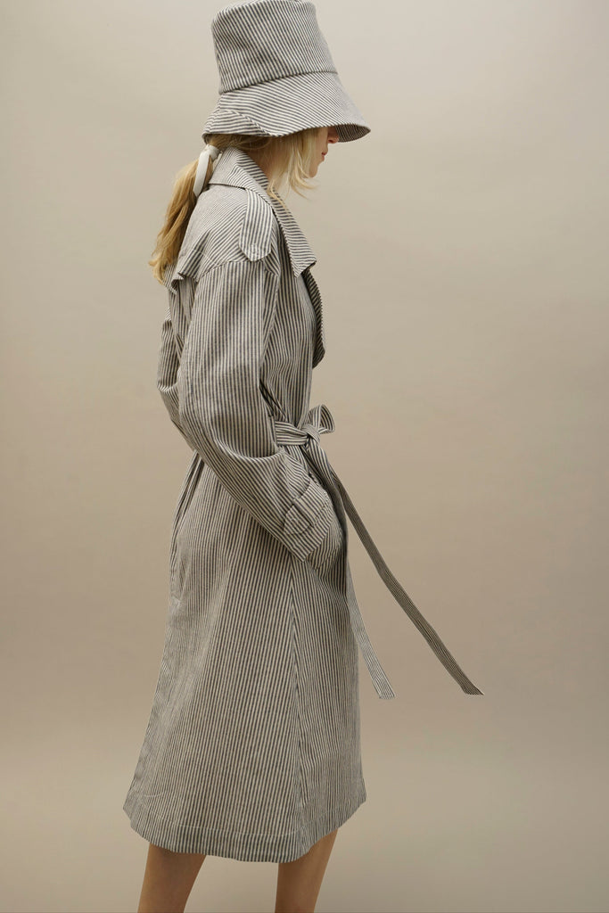 Profile of model wearing an organic cotton trench coat/dress in white and blue pinstripe by NINObrand