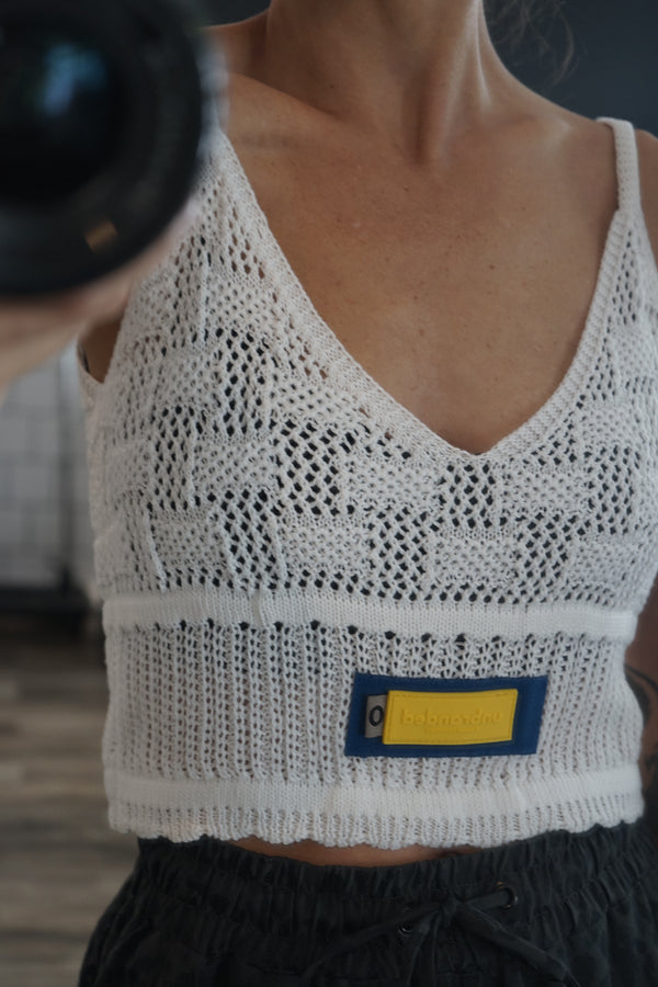 A close-up image focusing on the blue grosgrain ribbon and the yellow "Unbranded" label on the front of the white knit summer tank.