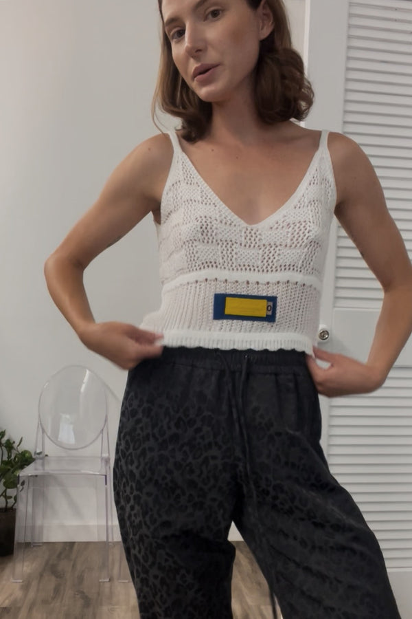 A model wearing a trendy white loose Knit Tank, with a rich designer label on the front.